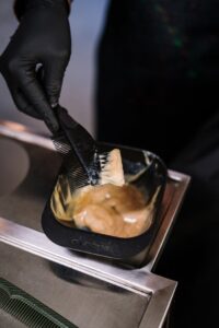 Close-up of stylist mixing hair dye with black brush in salon environment.