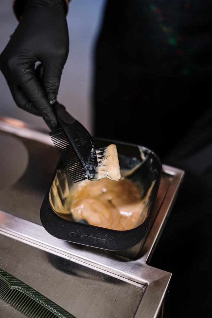 Close-up of stylist mixing hair dye with black brush in salon environment.